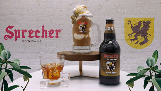 A glass of liquor, a bottle of root beer, and a root beer float in a mug on a pedestal with a sprecher logo in the background