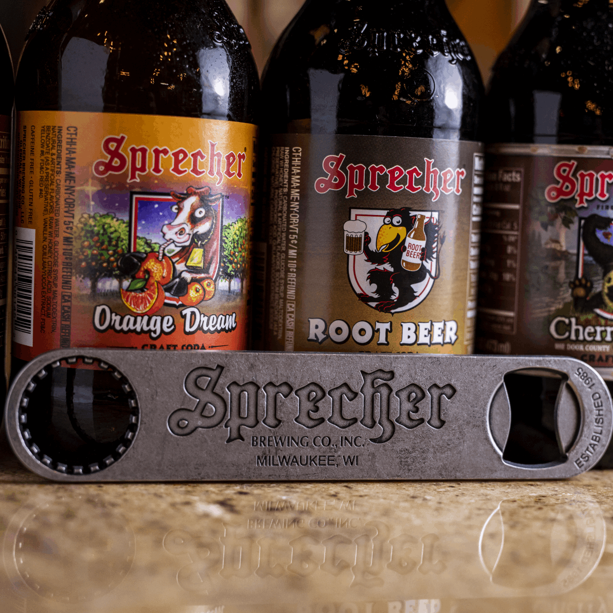 Sprecher pewter bottle opener with bottles of Sprecher Soda in the background