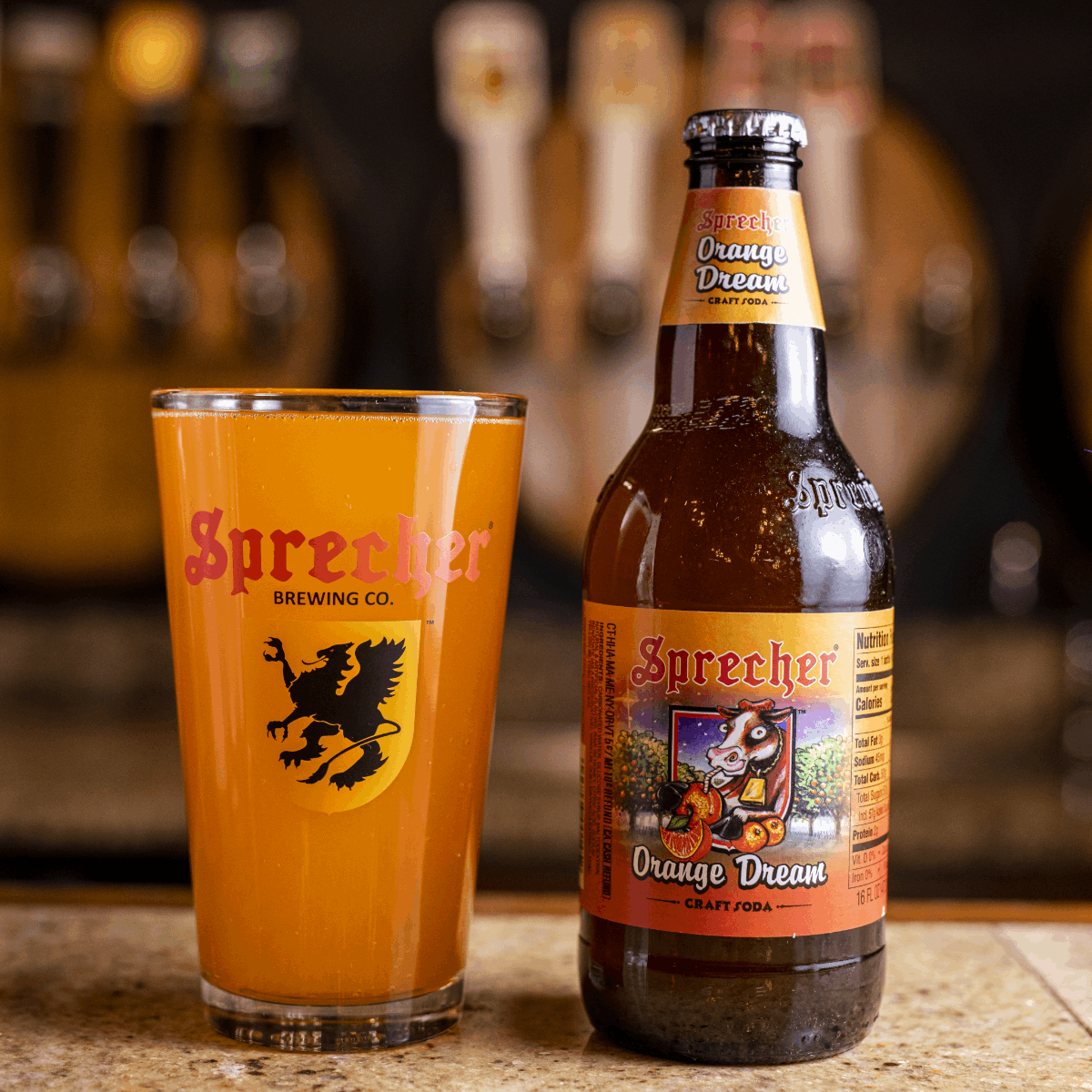 A glass and a bottle of Sprecher Orange Dream soda on a bar