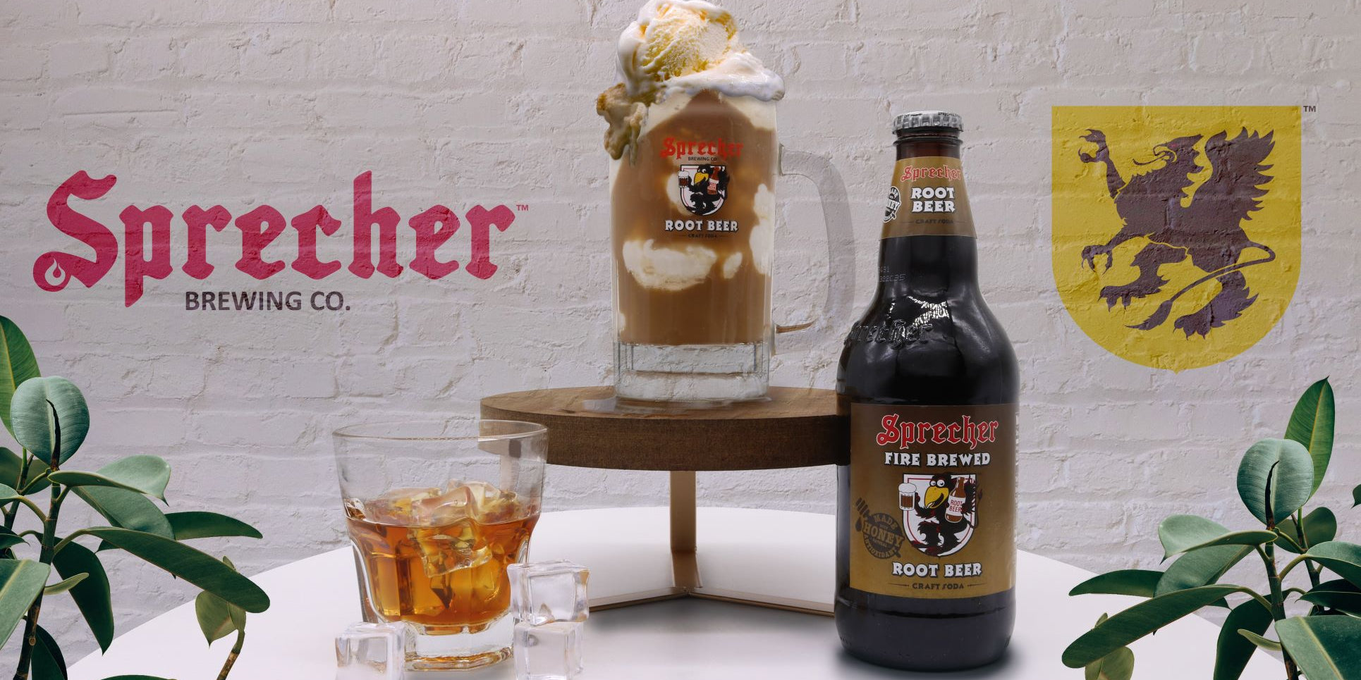 A glass of liquor, a bottle of root beer, and a root beer float in a mug on a pedestal with a sprecher logo in the background
