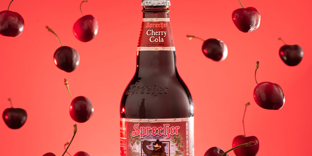 A 16oz bottle of Cherry Cola surrounded by falling cherries with a red background