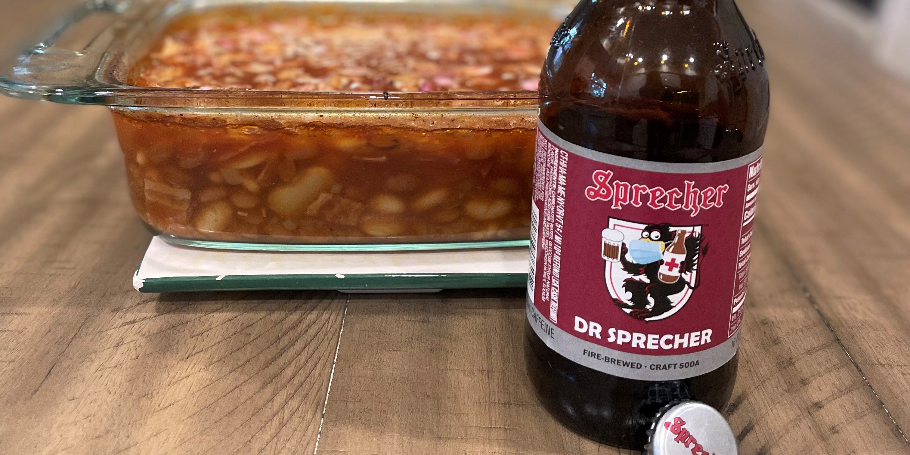 A glass pan of Dr Sprecher baked beans with a bottle of Dr Sprecher in the foreground