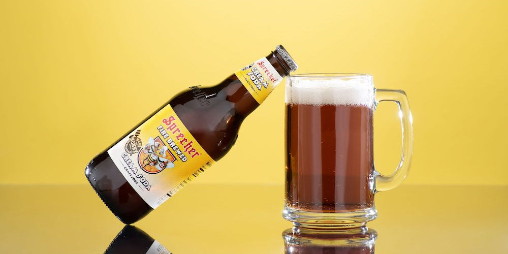 A bottle of Sprecher Cream Soda leaning on a mug of Cream Soda against a yellow background