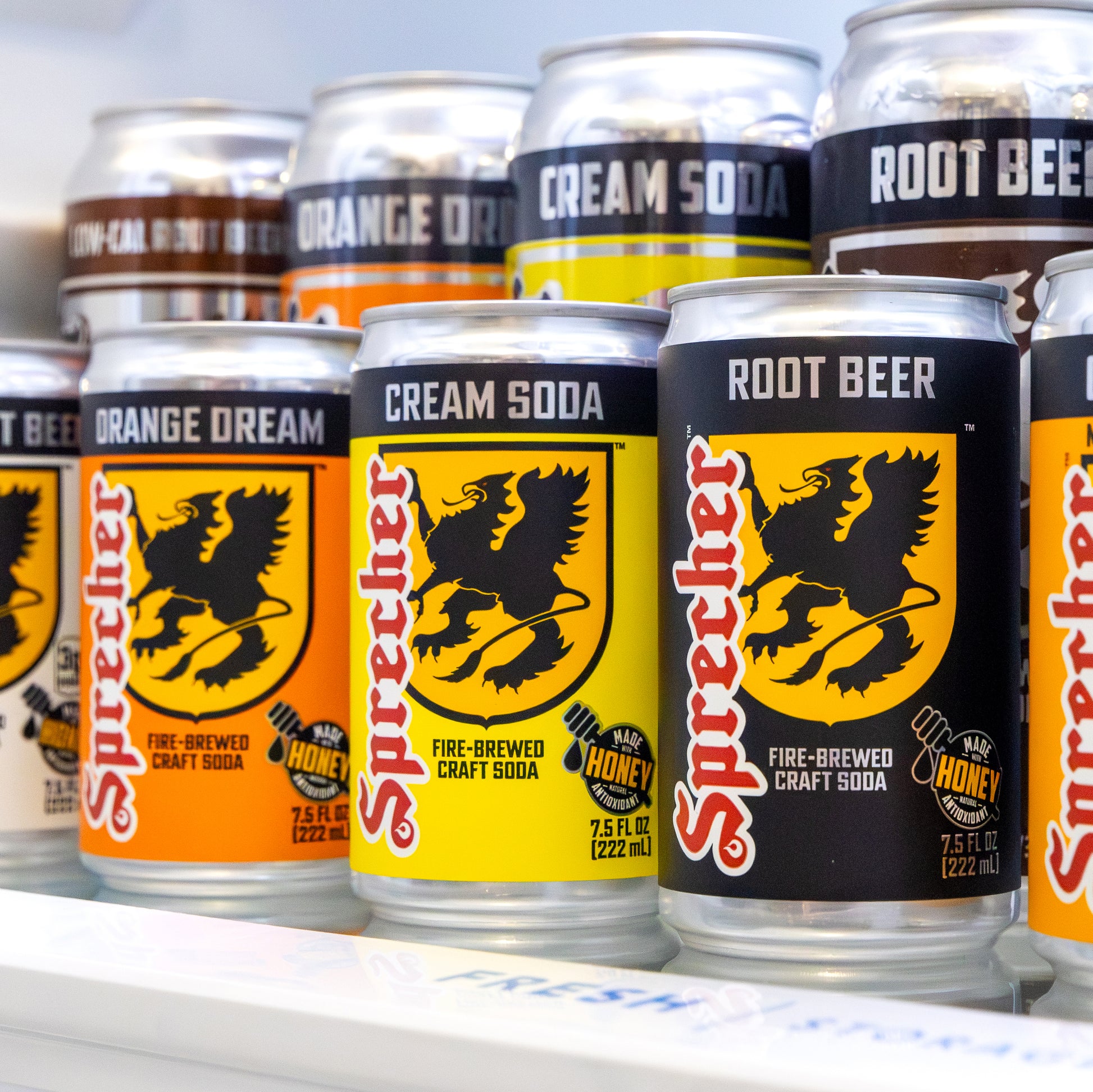 Multiple cans of Sprecher soda in various flavors on a white surface.