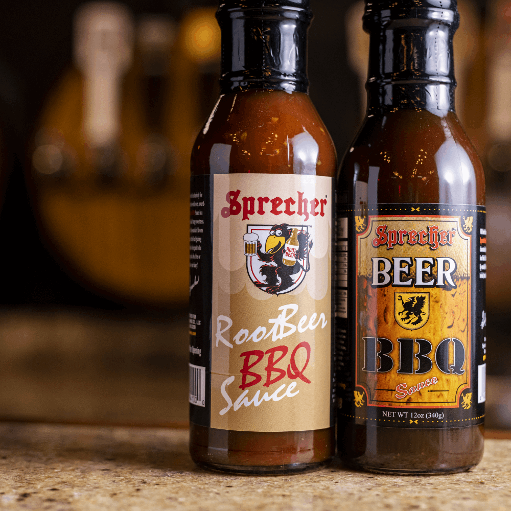 12oz bottles of Sprecher Root Beer BBQ Sauce and Beer BBQ Sauce next to each other on a bar.