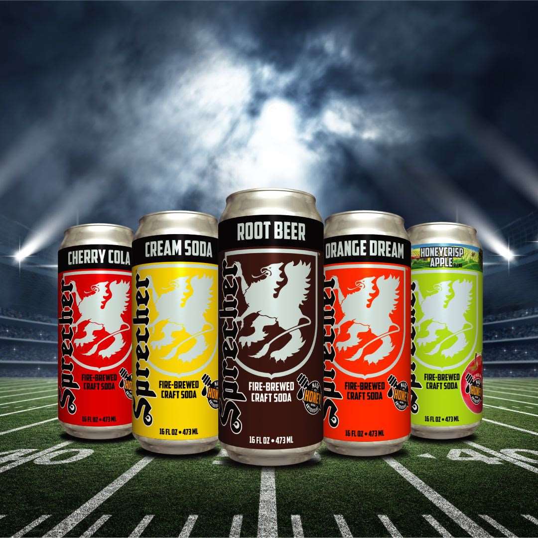 5 16oz cans of Sprecher Fire-Brewed Craft Soda on a football field with the sun breaking through dark clouds in the background. From left to right, cherry cola, cream soda, root beer, orange dream, and honeycrisp apple.