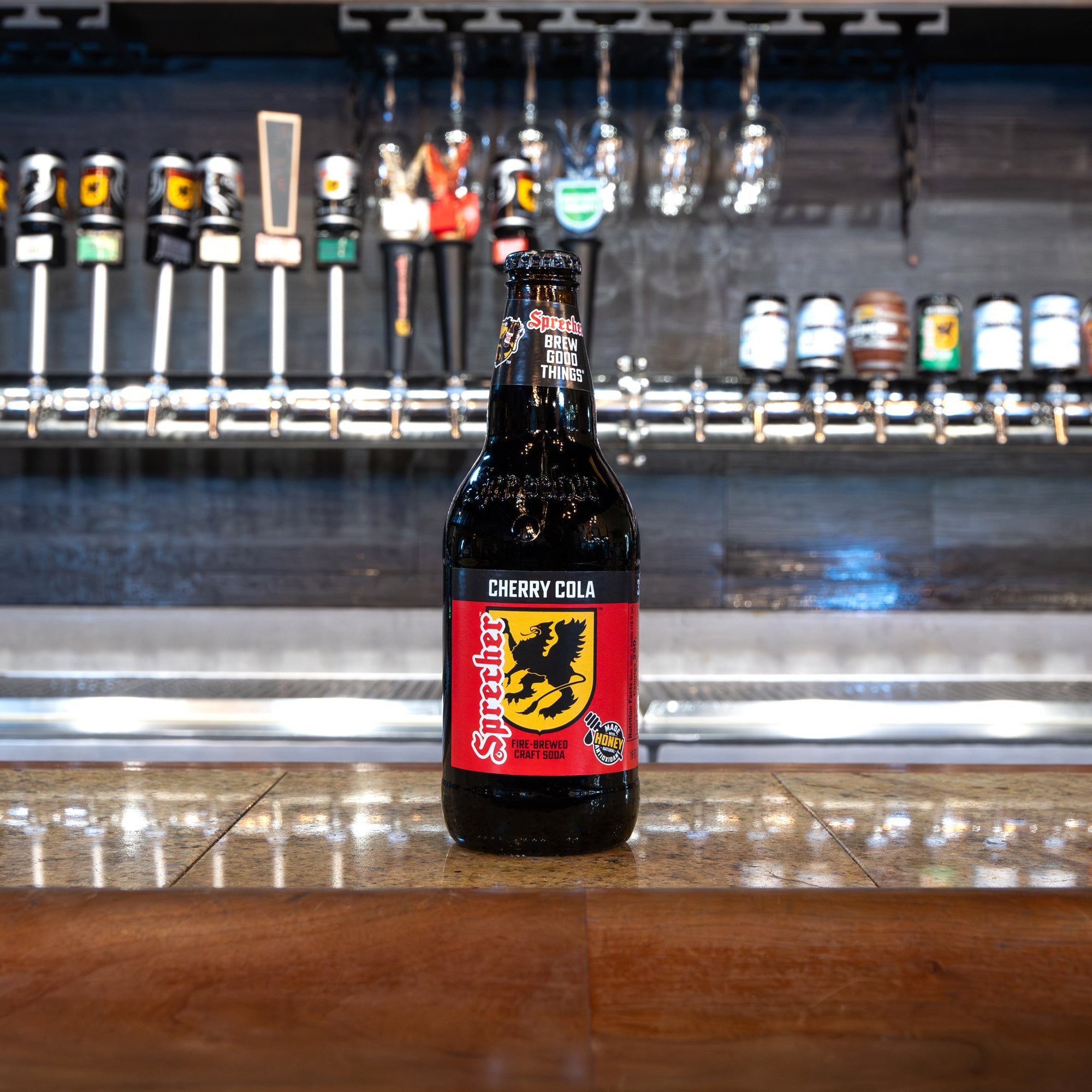 Bottle of Cherry Cola with a red label featuring a black bear on a bar counter with beer taps in the background.