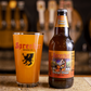 A pint glass of Sprecher Orange Dream next to a 16oz bottle of Orange Dream on a bar