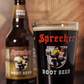 A pint glass of Sprecher Root Beer in the foreground with a blurry bottle of Sprecher Root Beer in the background