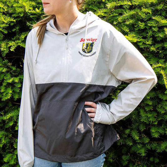 Woman wearing a two-tone windbreaker with the sprecher logo on the front, a front pocket, and an adjustable hood.