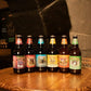16 oz bottles of Sprecher Grape, Cherry Cola, Puma Kola, Cream Soda, Orange Dream, and Ginger Ale next to each other on a barrel