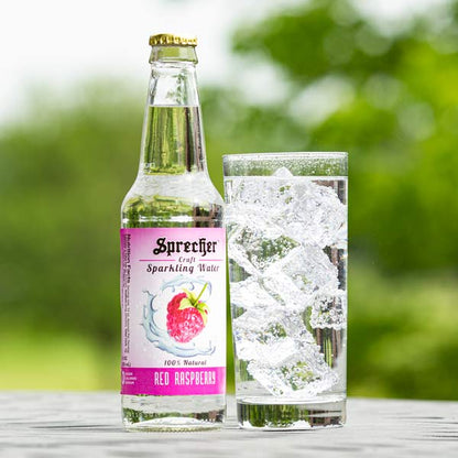 12oz bottle of Sprecher Red Raspberry Sparkling Water next to a glass of Sparkling Water outdoors.
