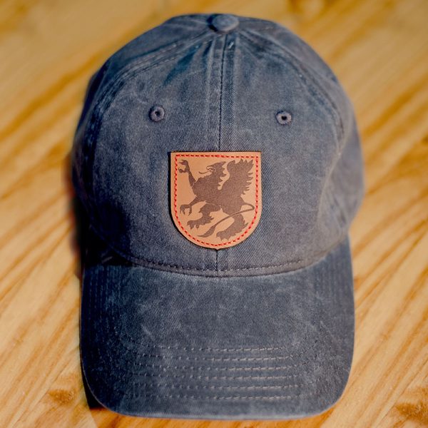 Sprecher Charcoal Baseball Hat with leather logo patch on a wood background